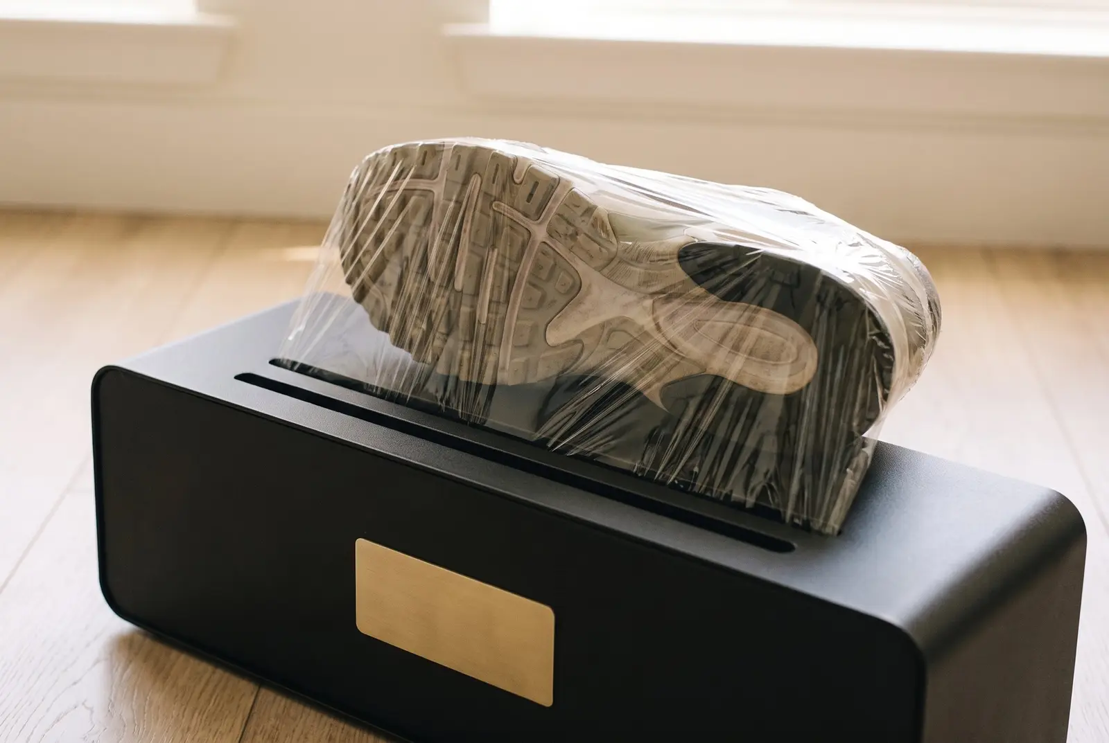 A sneaker sole on the TidySteps plate, clear film drawn tight over the tread and stopping at the edge of the sole.