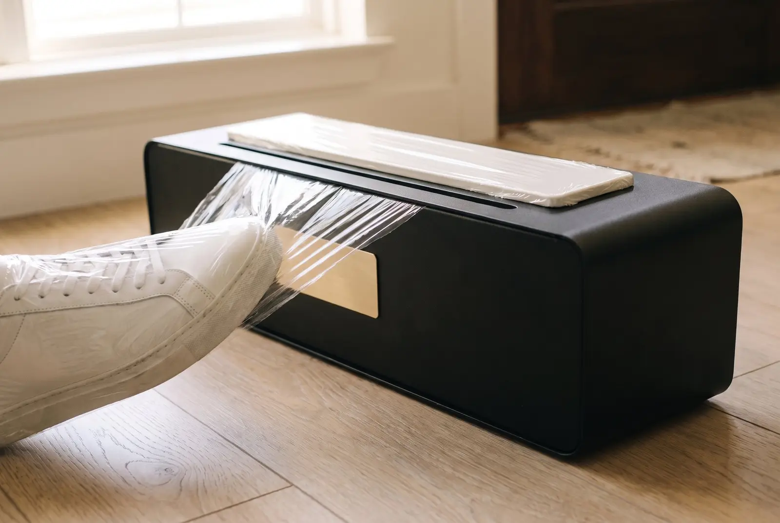A covered shoe stepping off the TidySteps unit onto a hardwood floor as the film separates at the tear edge.